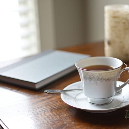 A cup of tea, a journal and a candle on a wooden table in morning light