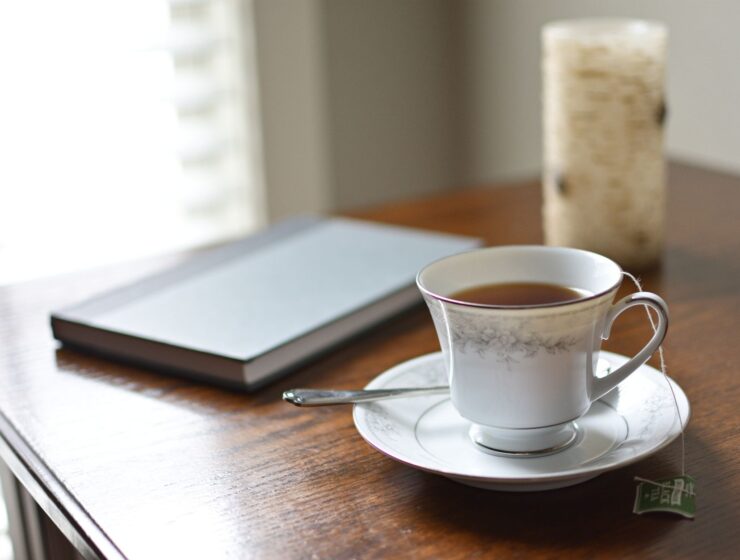 A cup of tea, a journal and a candle on a wooden table in morning light